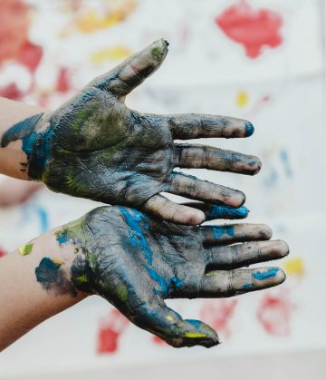 Händer med färg och tavla i bakgrunden