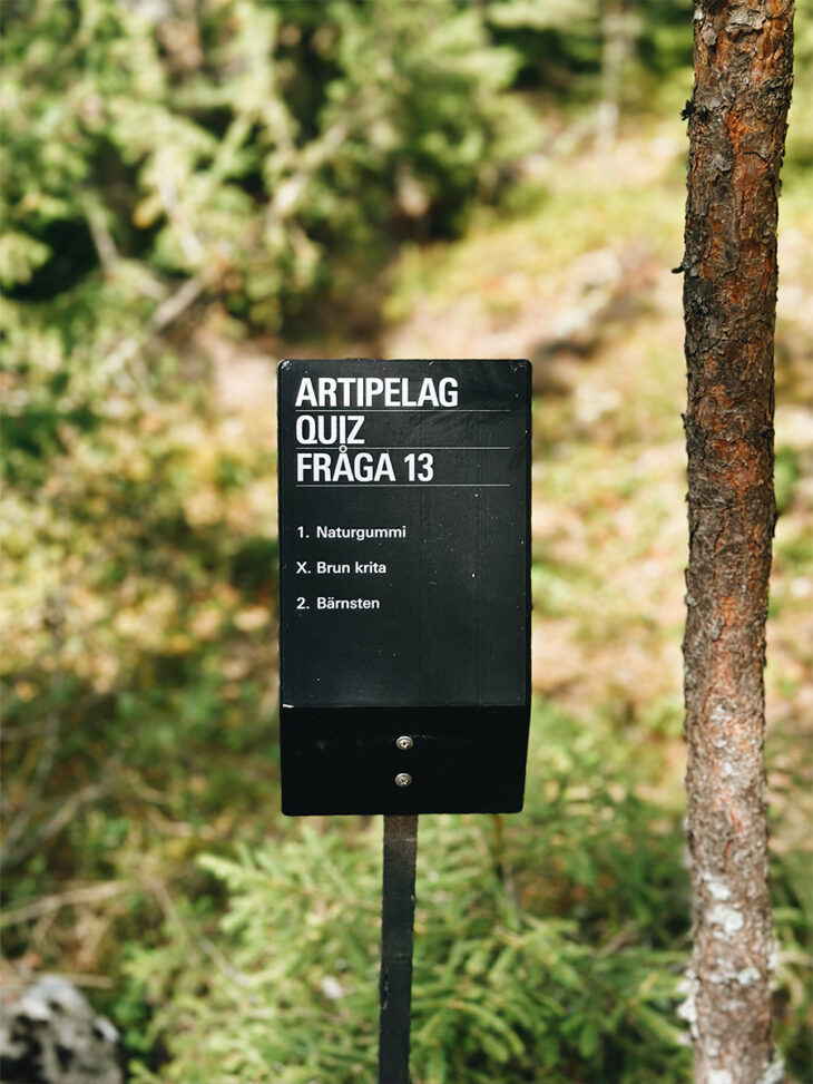 Bilden föreställer en skylt med en fråga från Artipelags tipspromenad. I bakgrunden skymtar skog.