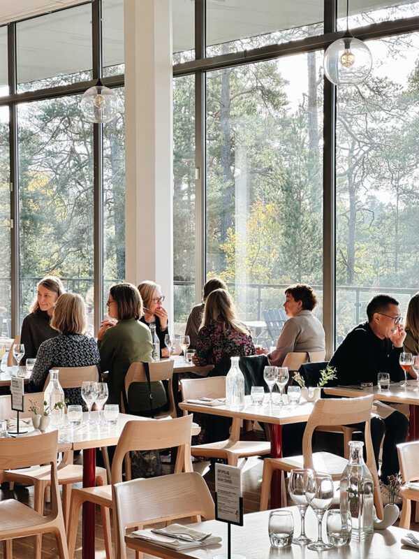 Folk njuter av en Art'n-brunch i den ljusa, moderna restaurangen med stora fönster med fridfull skogsutsikt, som erbjuder både konstupplevelse och läcker brunch.