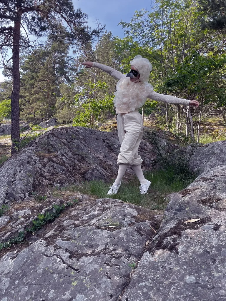 Person utklädd till fågel som dansar i skogen.