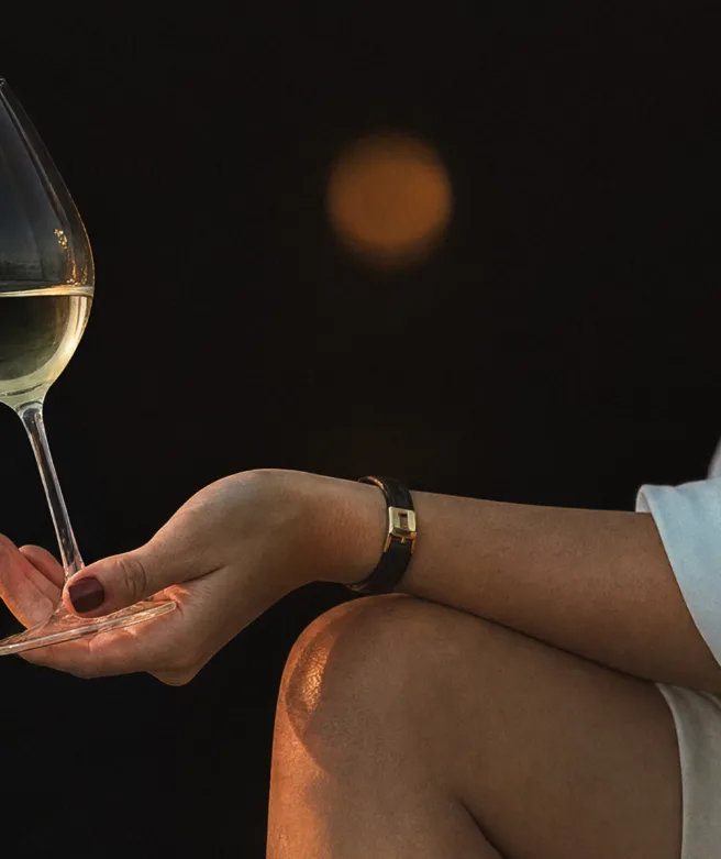 Bild på en kvinnas arm med ett glas vitt vin i handen.